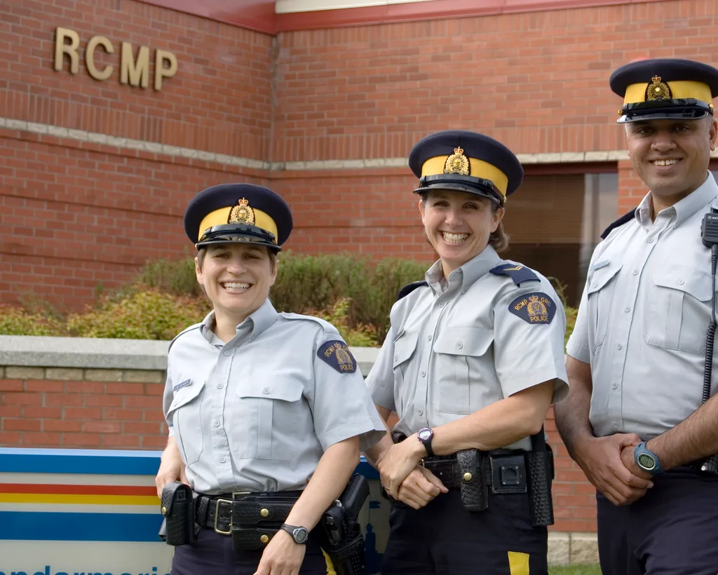 Three smiling RCMP officers in everyday working uniform outside a detachment